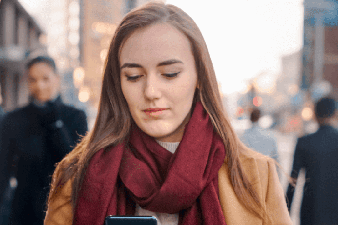 Young woman walking in the street while using her phone